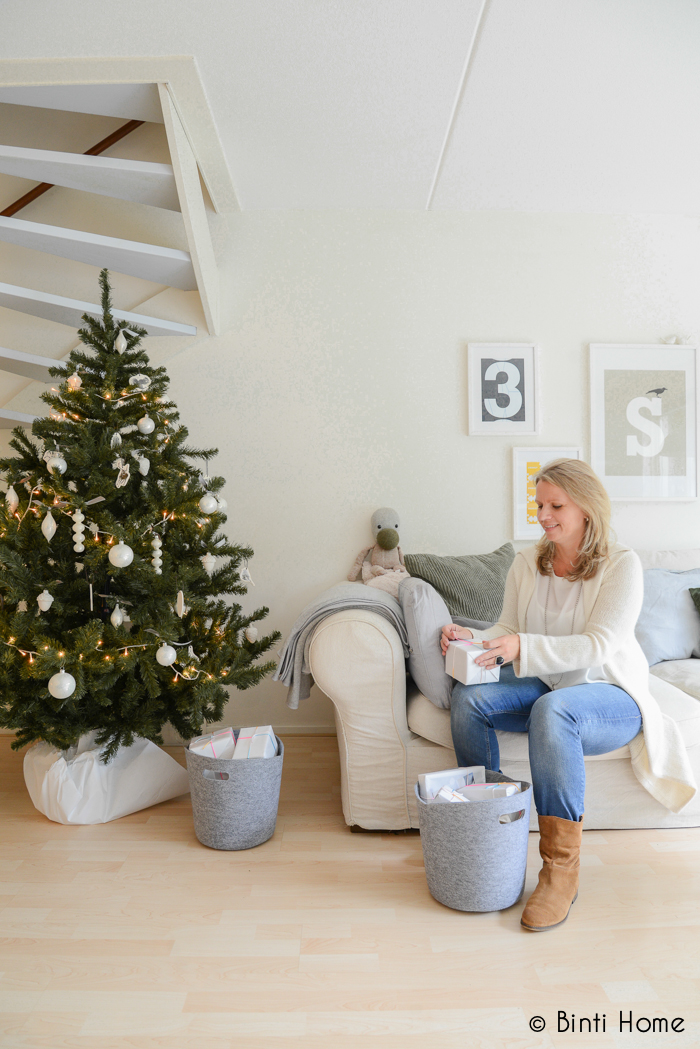 Woonkamer met lichte muren en versierde kerstboom met comfy bank en vilten manden met cadeautjes - via Accessorize your Home